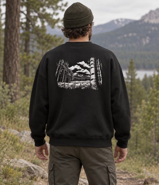 Man wearing black organic cotton sweatshirt with black and white forest and mountain artwork on the back